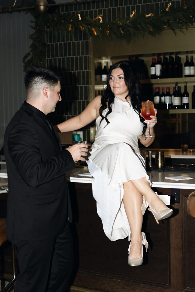 Bride and groom smiling while sitting on the bar at Hotel 1928.