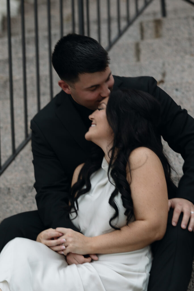 Couple laughing together while sitting on the steps of the historic Waco courthouse for portraits.