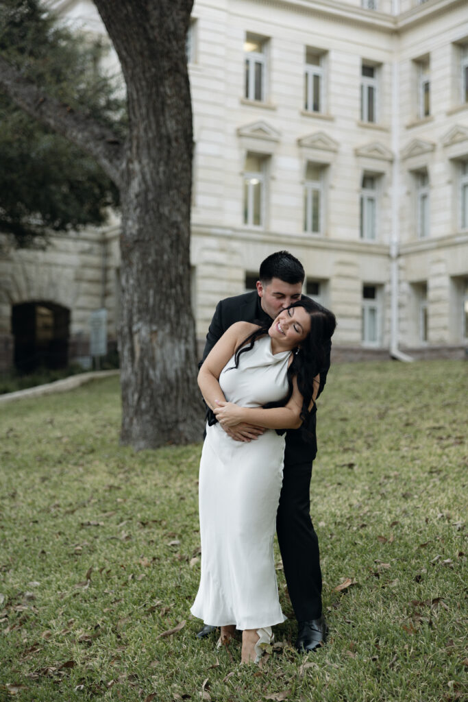 Bride and groom embracing on the Waco courthouse grounds, candid moment.