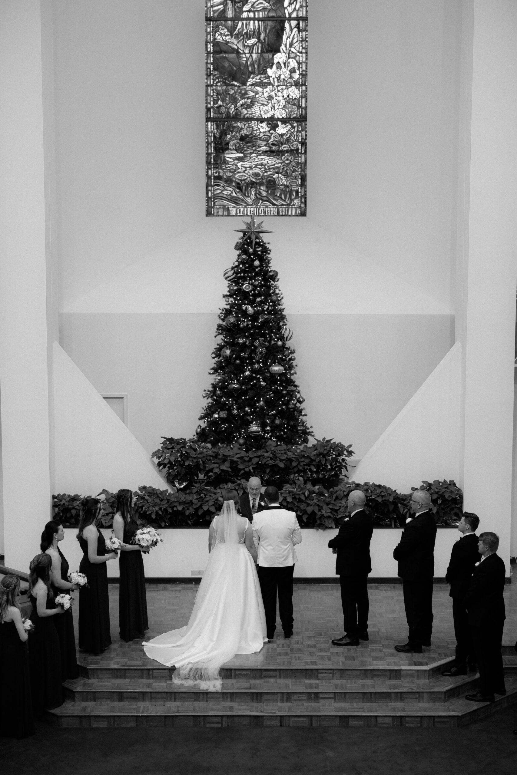 Black and white photo of a couple celebrating their Christmas wedding in Waco, Texas, standing beside a decorated Christmas tree with soft holiday lig